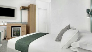 Quarto de hotel com cama, secretária com frigorífico, televisão e guarda-roupa.