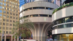 Uma praça urbana moderna com um espelho de água central, rodeada por edifícios contemporâneos.