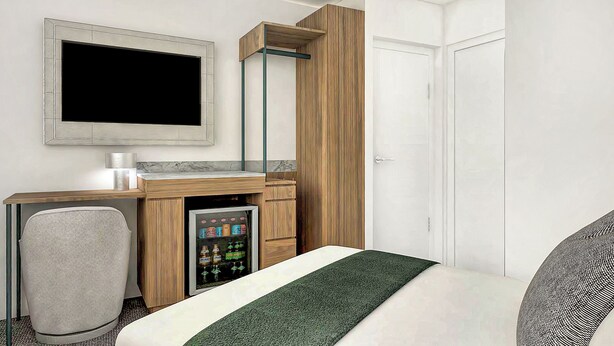 Quarto de hotel com cama, escrivaninha, computador, televisão, frigobar e porta.