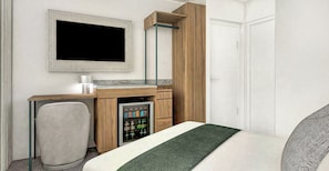 Ein Hotelzimmer mit Bett, Schreibtisch mit Computer, Fernseher, Minibar und einer Tür.