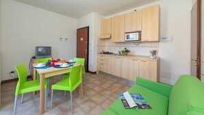 Ett kompakt bostadsutrymme med en matplats, ett litet kök och en grön soffa.