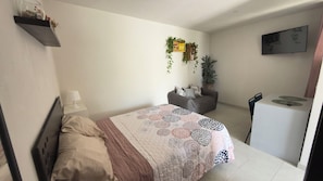 A bedroom with a bed, bedside table, lamp, and a small desk with a chair.