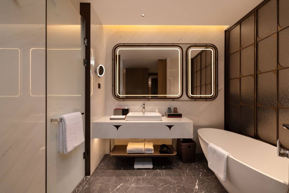 Un baño moderno con cabina de ducha de vidrio, un lavamanos blanco con espejo y una bañera independiente.