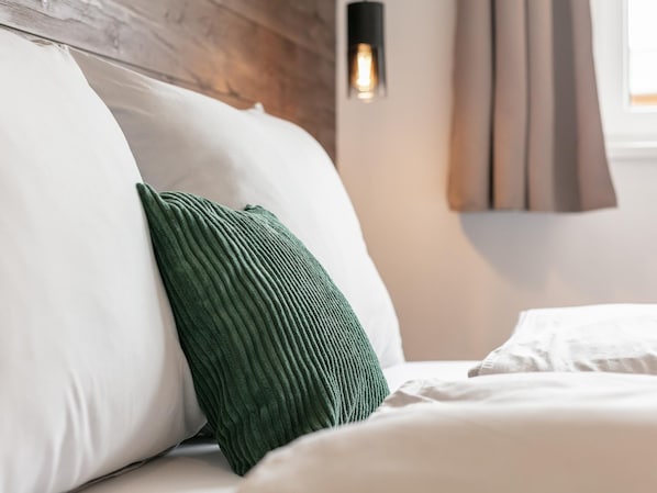 Un lit bien fait, avec du linge de lit blanc et un coussin vert.