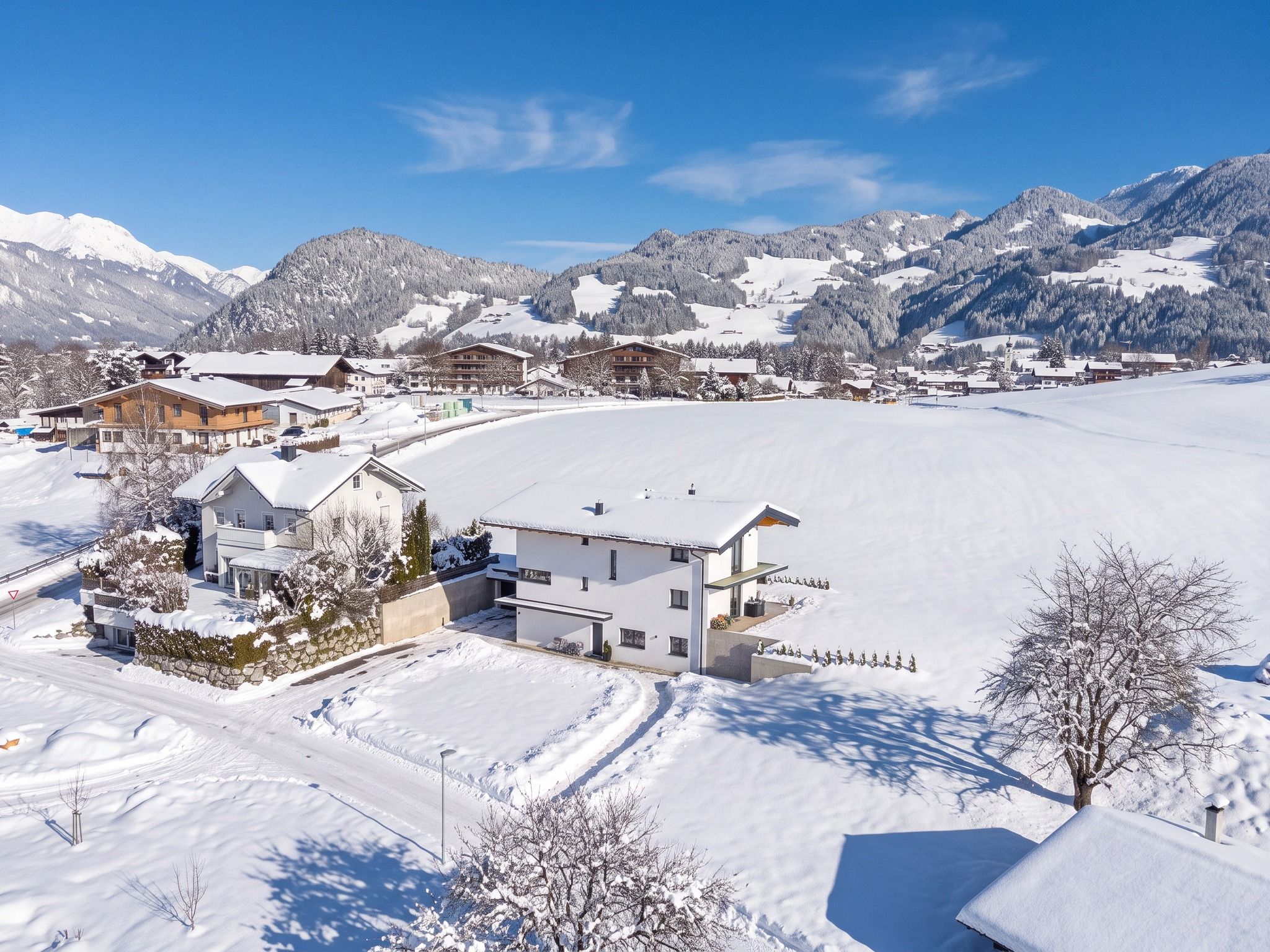 A snow-covered ski resort with modern buildings, a ski slope, and mountainous terrain in the background.
