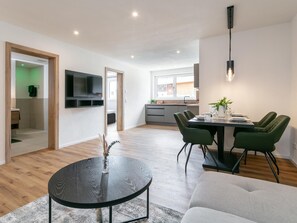 A modern kitchen with a dining area, a TV mounted on the wall, and a dining table with chairs.