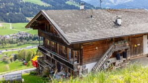 A wooden chalet with a balcony, a staircase, and a view of a valley and mountains. - Vacation apartment with a wide view & garden (Brixen)