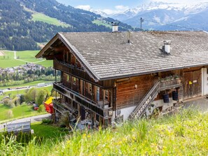 A wooden chalet with a balcony, a staircase, and a view of a valley and mountains.