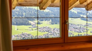 A wooden-framed window with a view of a town and forested hills. - Vacation apartment with a wide view & garden (Brixen)