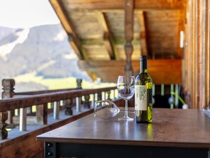 A wooden table with a wine bottle and two glasses on a balcony overlooking a mountainous landscape.