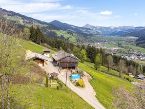 A rural house with a swimming pool, surrounded by green fields and mountains.