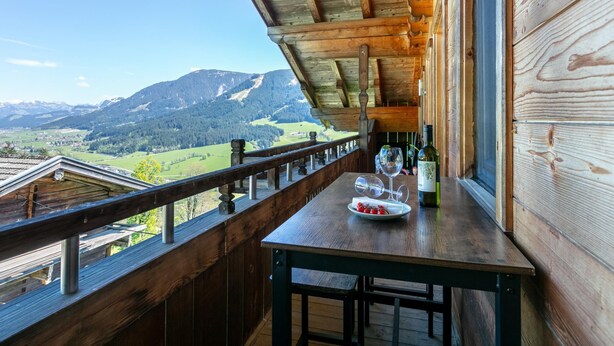 A wooden balcony with a table, wine glasses, and a bottle, overlooking a mountainous landscape. - Vacation apartment with a wide view & garden (Brixen)