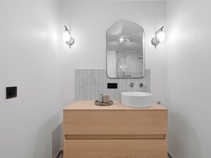 Ein modernes Badezimmer mit einem Holzbadezimmerhocker, einem runden Waschbecken, einem Spiegel und zwei Wandleuchten.