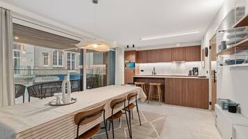 A modern kitchen with a dining area, large windows, and a view of the street.