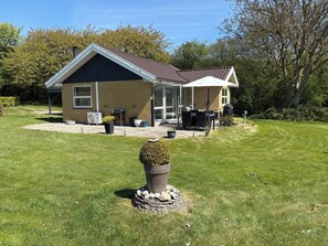 Een huis met een overdekt terras, een gazon en een klein tuinelement.