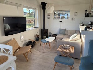 Een moderne woonkamer met een flatscreen televisie, een bank, een salontafel, rieten stoelen en een houtkachel.
