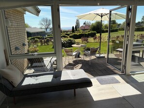 Eine sonnendurchflutete Terrasse mit Sitzgelegenheiten, einem runden Tisch und einem Sonnenschirm.