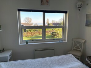 A bedroom with a large window, a radiator, a bed with a patterned bedspread, a chair, and a small table with a plant. - Lovely, secluded holiday home near beach (Sydals)