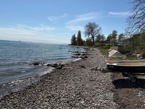 Ein Kiesstrand mit einem Boot am rechten Rand, einem klaren Himmel und ruhigem Wasser.