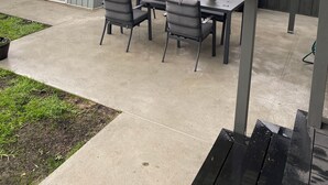 An outdoor patio with a table and chairs, a hanging planter with flowers, and a grill.