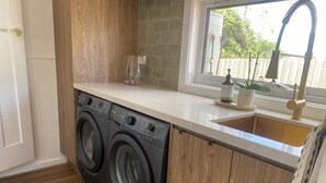 A compact laundry area with a washing machine, a sink, and a window with a view of a fence and trees.