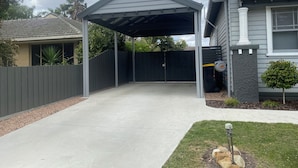 A covered patio area with a concrete floor, a black fence, and a small tree.
