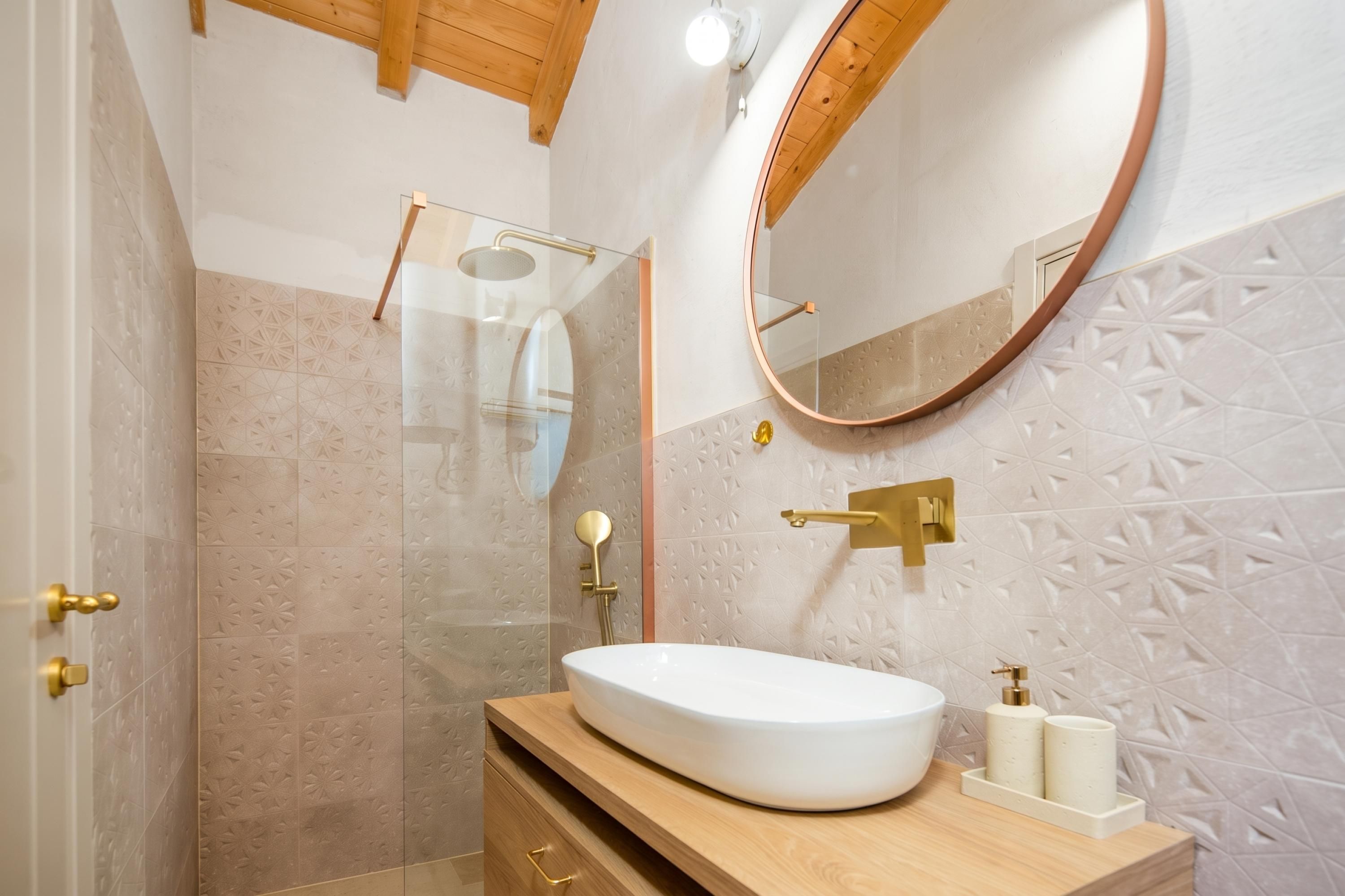 Un bagno con un lavandino bianco, uno specchio rotondo e una doccia con porta in vetro.