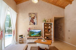 A cozy living room with a wooden ceiling, a painting on the wall, a television, a small table, and a bookshelf. - Villa Stonica - Rustic Istrian Pool Retreat (Tinjan)