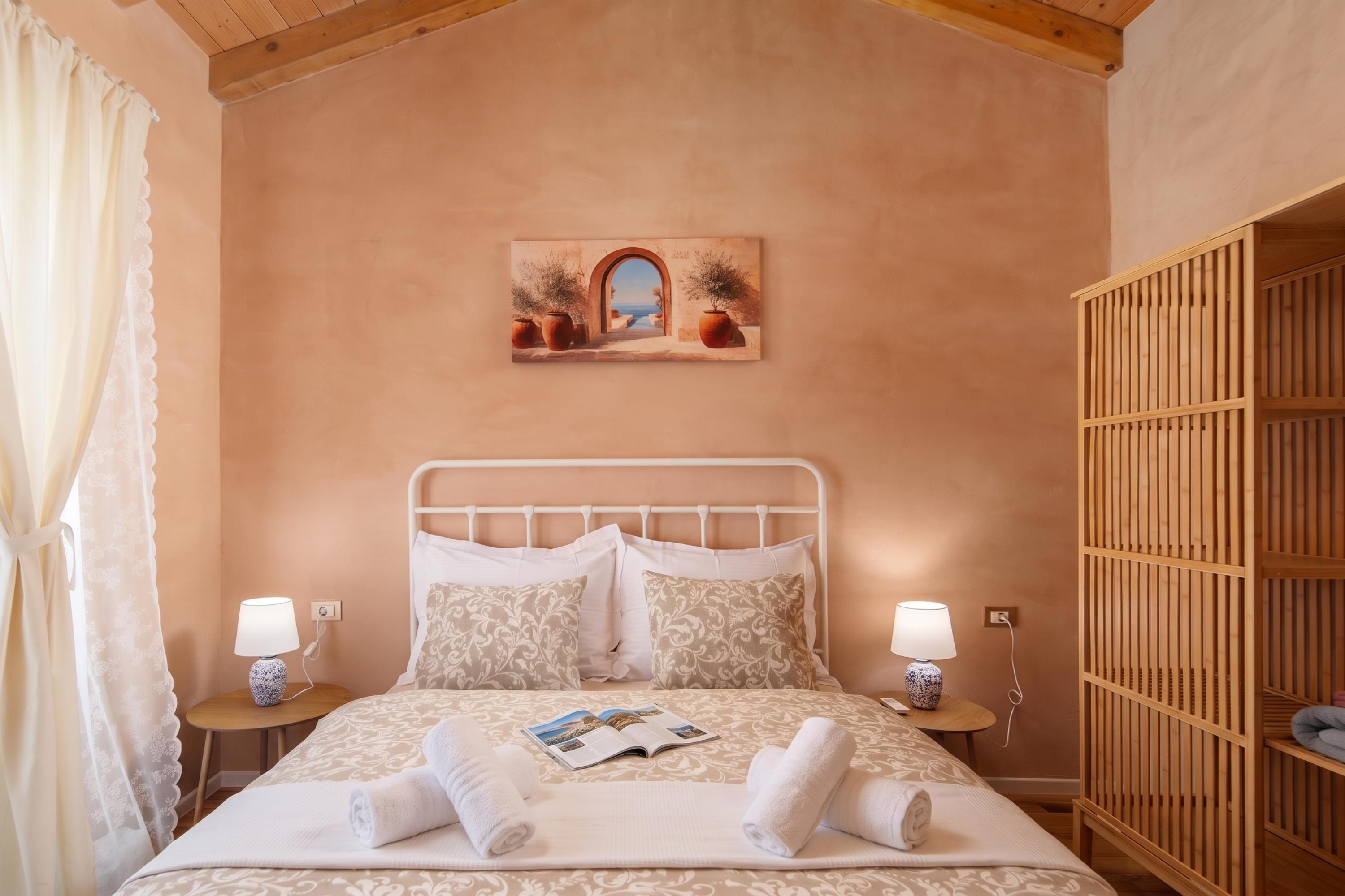 A bedroom with a bed, two bedside tables, a nightstand, a wooden wardrobe, and a painting on the wall.