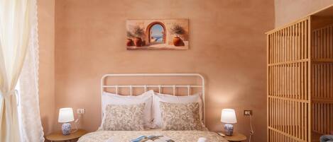 A bedroom with a bed, two bedside tables, a nightstand, a wooden wardrobe, and a painting on the wall.