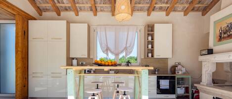A modern kitchen with wooden beams, a central island with stools, and a window with a view.