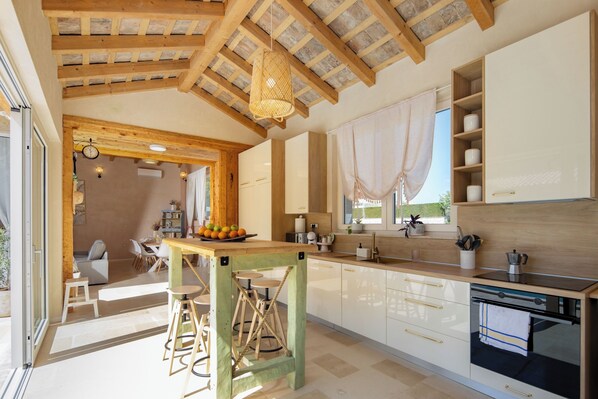 A modern kitchen with wooden beams, a large window, and a dining area with a table and chairs. - Villa Stonica - Rustic Istrian Pool Retreat (Tinjan)