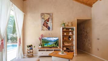 A cozy living room with a wooden ceiling, a painting on the wall, a television, a small table, and a bookshelf.