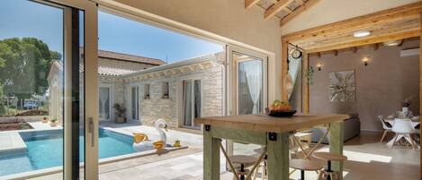 Un interior moderno con vista a la piscina, vigas de madera en el techo y un comedor con taburetes.
