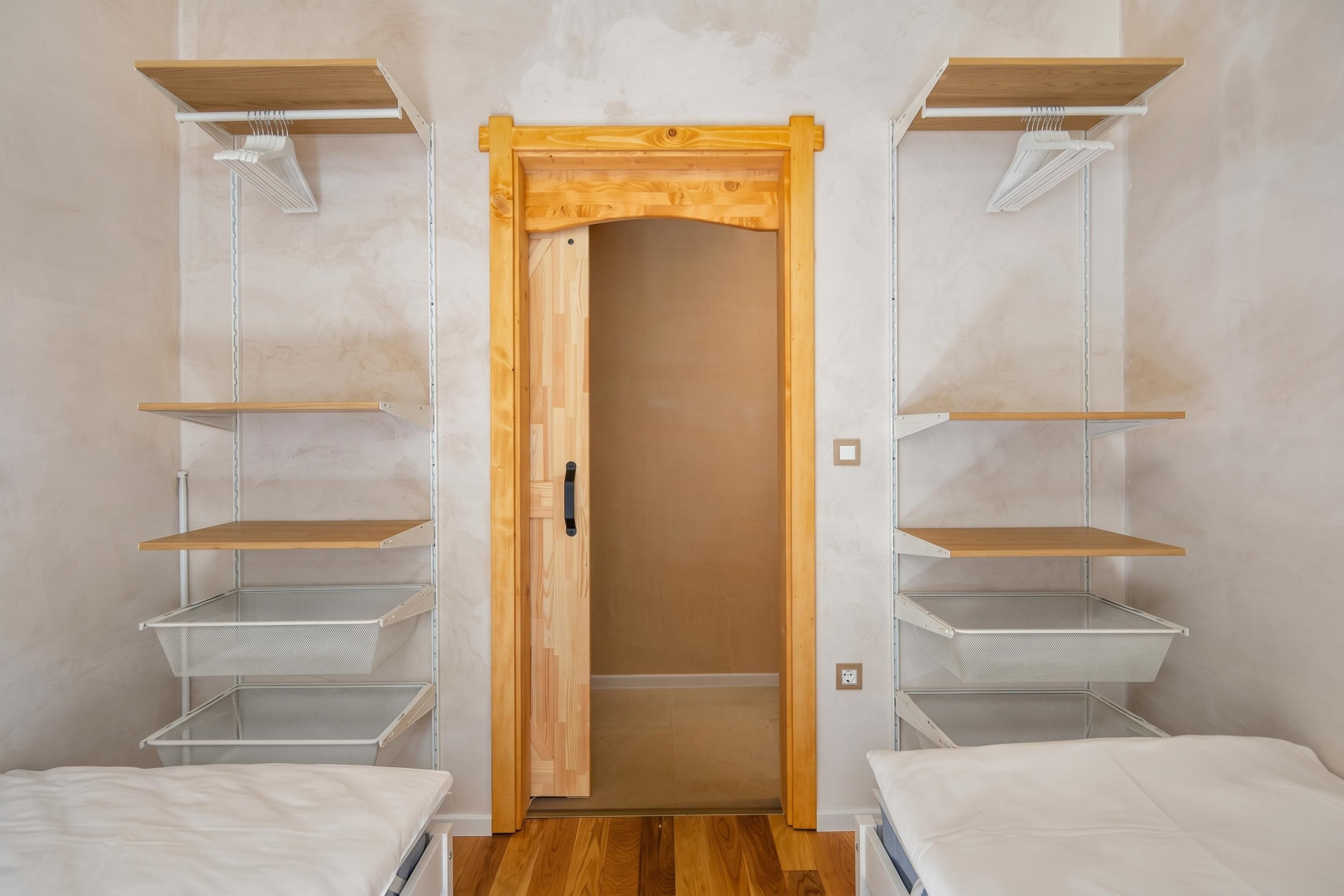 Quarto com guarda-roupa de madeira, duas prateleiras de metal e uma cama.