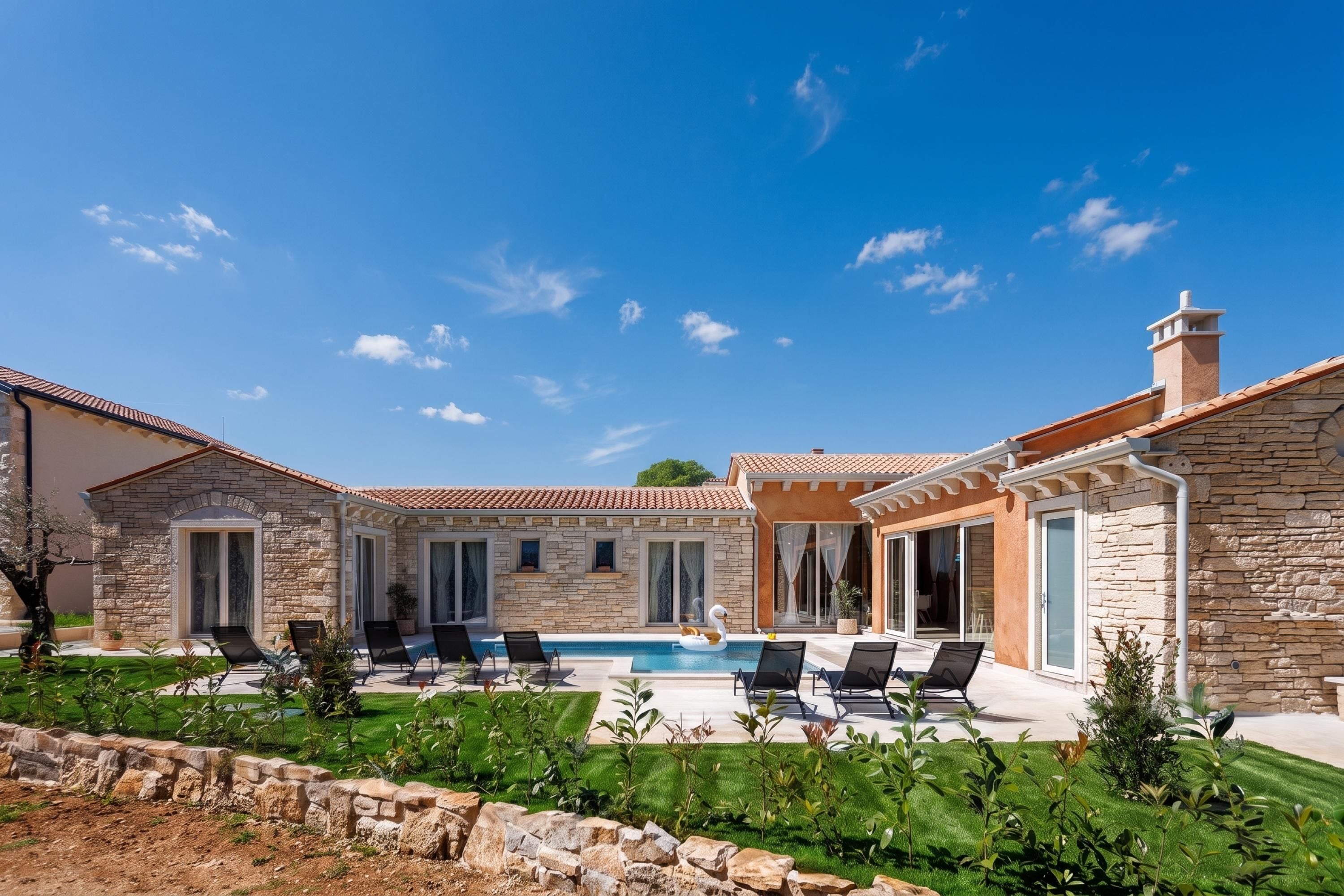 Una villa de piedra con piscina, mobiliario de exterior y un jardín cuidado.
