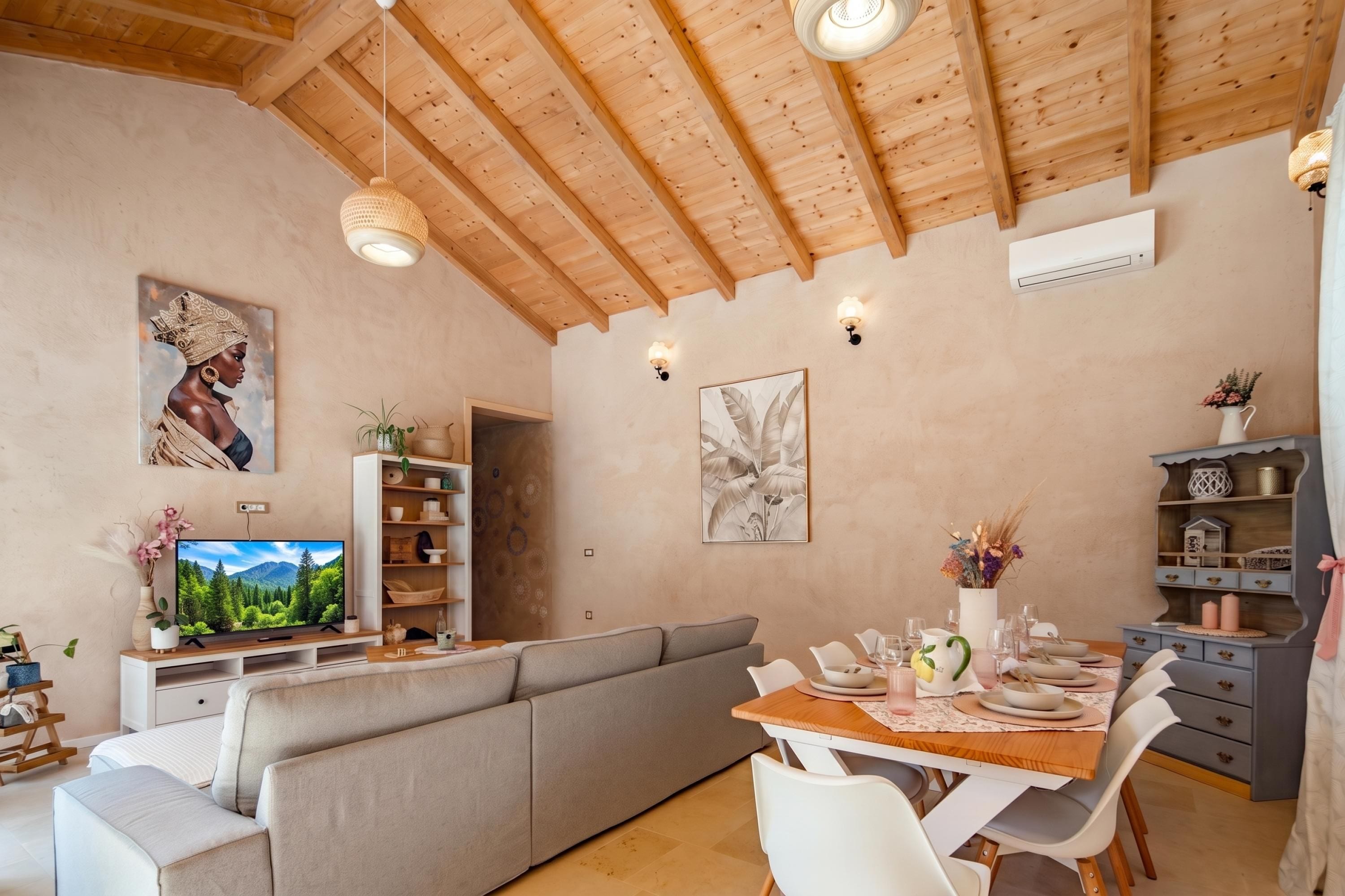 Una sala moderna con techo de madera, televisor, sofá, mesa de comedor para dos personas y estantería.