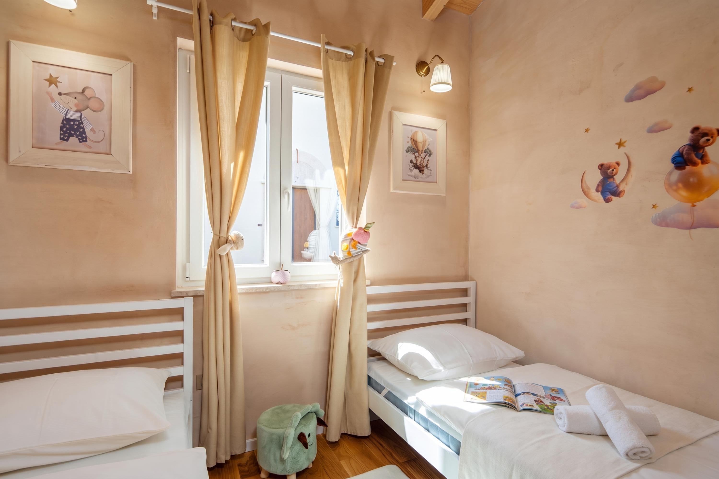 Habitación infantil con literas, una ventana con cortinas y adornos de pared que incluyen un ratón y un globo aerostático.