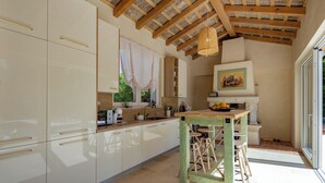 A kitchen with white cabinets, a wooden ceiling, and a dining area with stools. - Villa Stonica - Rustic Istrian Pool Retreat (Tinjan)