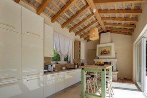 Una cocina con armarios blancos, techo de madera y un comedor con taburetes.