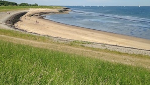 En strand med en böljande kustlinje, gräsbevuxna områden och en klar himmel.