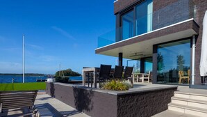 Un edificio moderno con un balcone, posti a sedere all'aperto e vista sull'acqua.