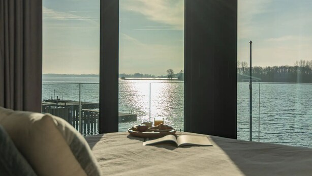 Una stanza con un'ampia finestra vista su un corpo d'acqua, un letto e un libro sul davanzale.