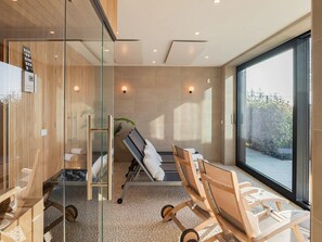 Ein modernes Badezimmer mit Glastrennwand, einem Holzkosmetikschrank, einem Massagesessel und einem großen Fenster.