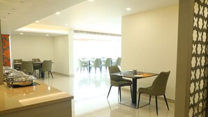 Un lobby moderno de hotel con una mesa de recepción, varias mesas de comedor y sillas.