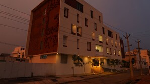 Un edificio de varios pisos con un diseño arquitectónico moderno, que presenta una combinación de ventanas rectangulares y cuadradas, una entrada visible con escalones y un techo plano.