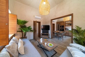 Ein modernes Wohnzimmer mit einer Couch, einem Couchtisch und einem Fernseher. Es gibt eine Küchenzeile mit einem Esstisch und Stühlen.