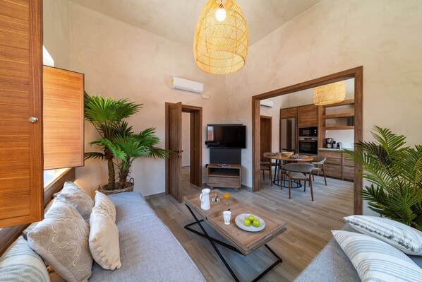 Ein modernes Wohnzimmer mit einer Couch, einem Couchtisch und einem Fernseher. Es gibt eine Küchenzeile mit einem Esstisch und Stühlen.