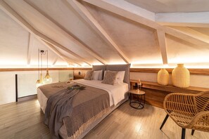 Ein Schlafzimmer mit schrägen Wänden, einem Bett mit gemustertem Überwurf, einem kleinen runden Tisch und Korbstühlen.