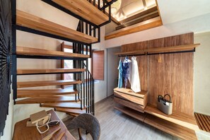Un interior moderno con una escalera de madera, un perchero y un banco con un bolso.